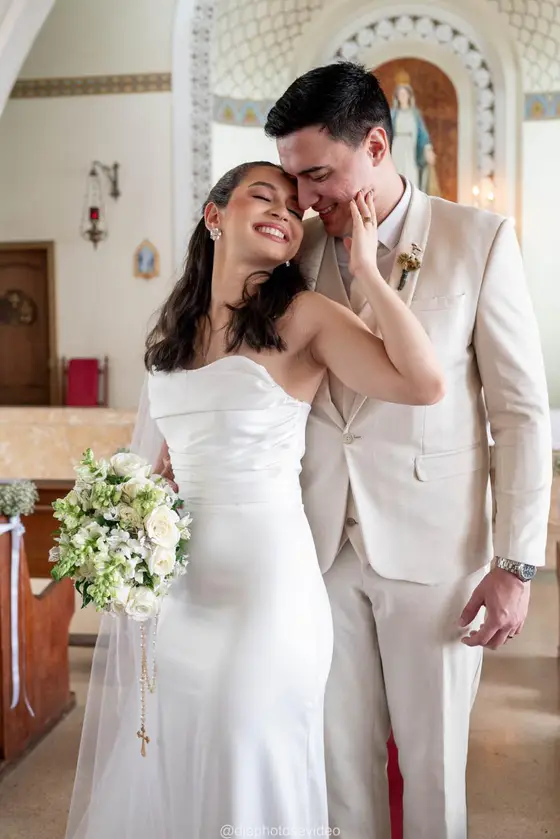 Noivos sorrindo dentro da igreja, ele beija a testa dela