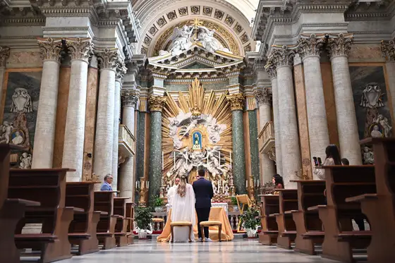 Casamento em Roma: noivos no altar de uma igreja ornamentada, vistos do fundo da nave