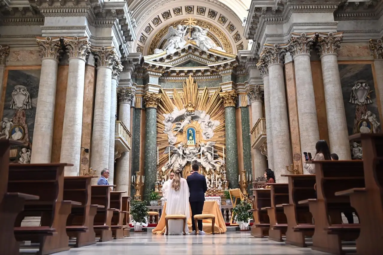 Casamento em Roma: noivos no altar de uma igreja ornamentada, vistos do fundo da nave