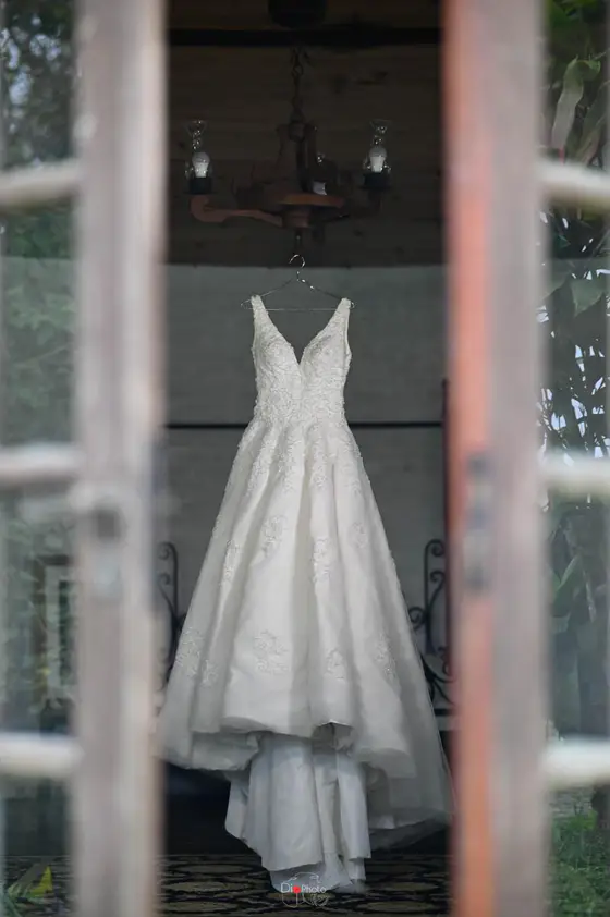 Vestido de noiva pendurado, visto pela janela de madeira