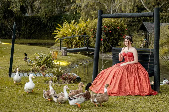 Debutante de vestido vermelho no balanço do jardim, com patos em volta